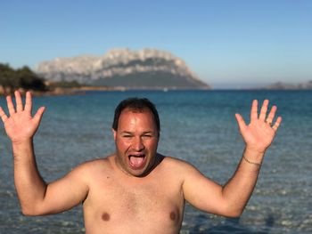 Portrait of shirtless mid adult man shouting while standing against sea