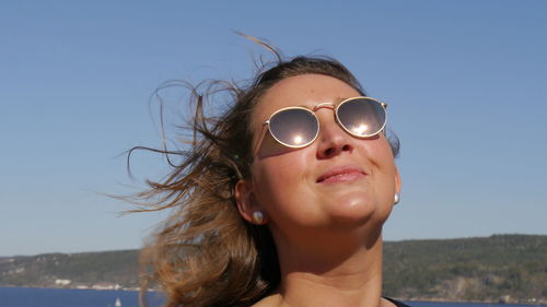 Close-up portrait of woman wearing sunglasses against clear blue sky