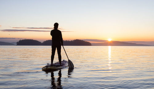 Silhouette man standing in sea against sky during sunset