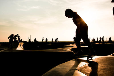 Silhouette woman skateboarding against sky at park during sunset