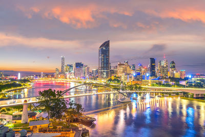 Illuminated buildings by river against sky at night