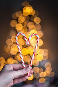 Hand holding two candy canes in heart shape with lights in background.