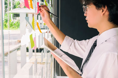 Side view of businessman writing on adhesive note in office