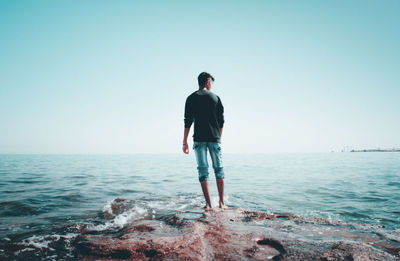 Rear view of man looking at sea against clear sky