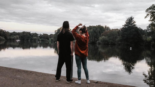 Rear view of people photographing lake against sky