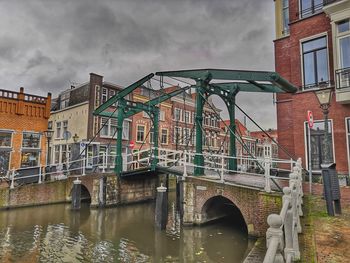 Bridge over river by buildings against sky