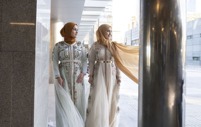 Fashionable female friends wearing fashionable dress standing on footpath