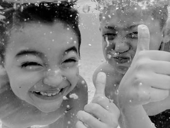 Portrait of smiling boys gesturing thumbs up while swimming in pool