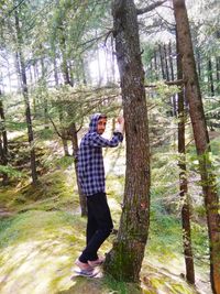 Full length of man standing by tree trunk in forest