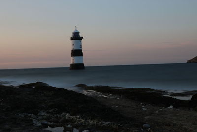 Lighthouse by sea against sky during sunset