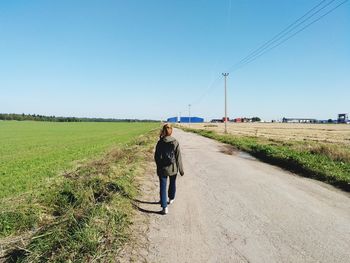 Rear view of woman walking on road amidst field