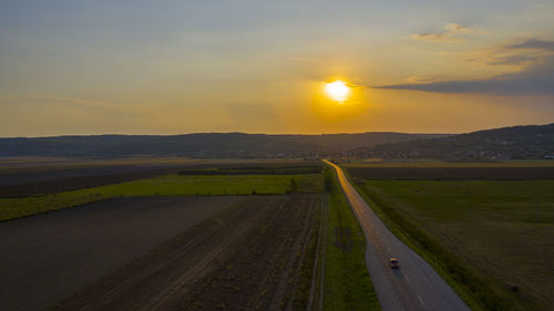 Scenic view of road amidst field against sky during sunset