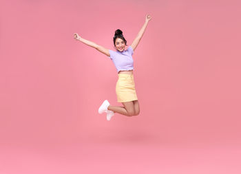 Full length of young woman jumping over pink background