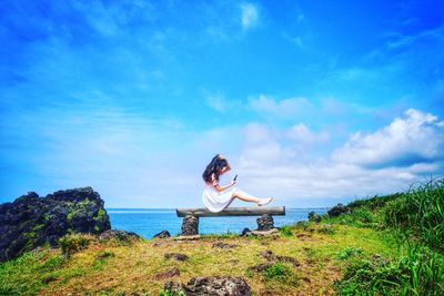 Woman sitting against blue sky and plants