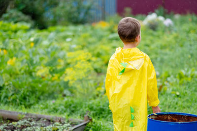 A boy in a yellow raincoat walks in the rain, back view. a child on the street