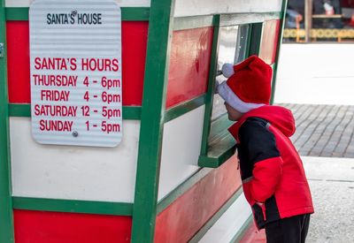 Little boy wearing a santa hat, looks in through the window to see if santa is there inside