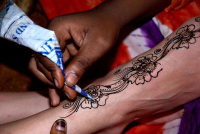 Cropped image of artist applying henna tattoo on woman leg