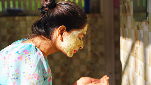 Beautiful woman is washing facial mask. girl spraying water on her face standing in front of mirror