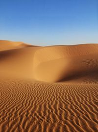 Sand dunes in desert against clear blue sky