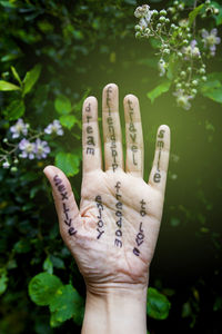 Cropped hand with texts on palm against plants