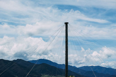 Low angle view of cables attached to pole against cloudy sky