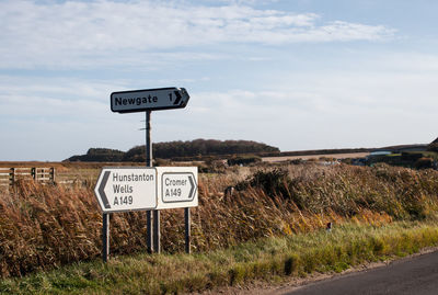 Information sign on road by field against sky