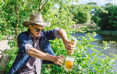 Man pouring beer in glass against plants