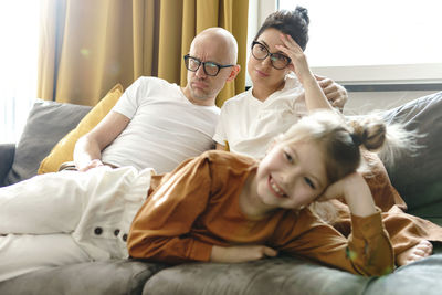 Happy daughter watching movie with unhappy parents at home