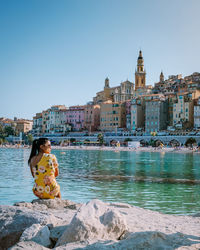 Man sitting on water by buildings against clear sky