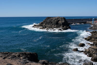 Scenic view of rocks in sea against clear blue sky