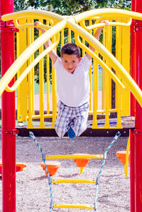 Young boy hanging from a bars on a colorful playground