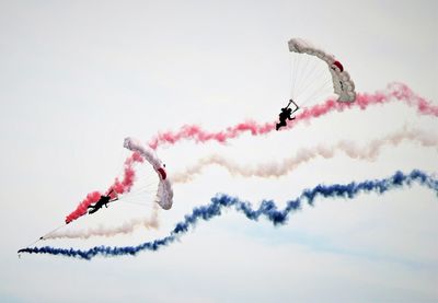 Low angle view of airshow with people parasailing against sky