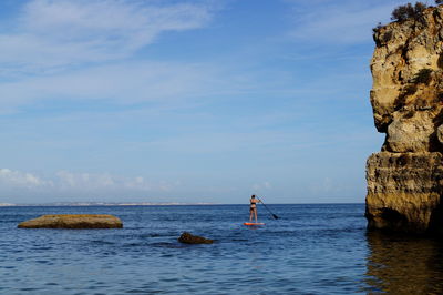 Rear view of woman paddleboarding on sea against sky