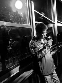 Man looking at camera while standing by window at night