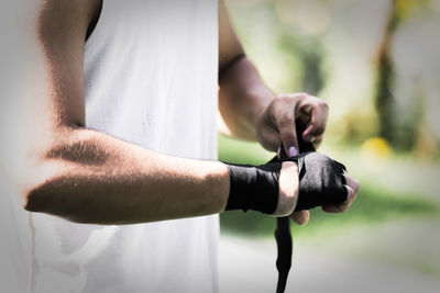 Midsection of boxer tying bandage while standing outdoors