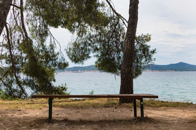 Bench by lake against sky