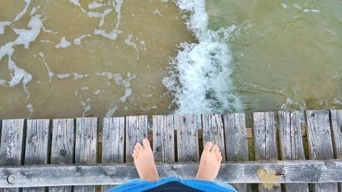 Low section of man standing on pier over river