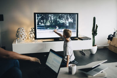 Full length of boy kneeling while touching smart tv in living room at home