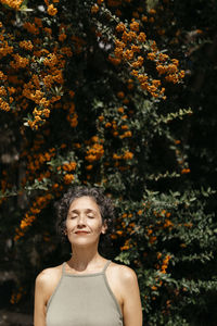 Mature woman with eyes closed standing against orange tree on sunny day