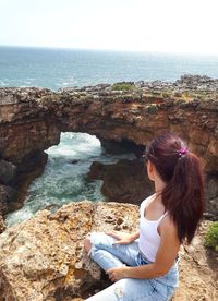 Woman sitting on rock by sea against sky