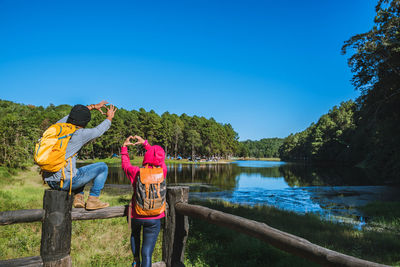 Woman standing by lake against clear blue sky