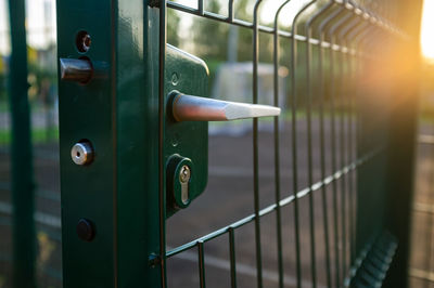 Handle with lock on open gate of sports ground fenced with a welded mesh fence outdoors at sunset