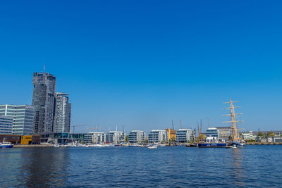 Sailboats in sea by modern buildings against clear blue sky