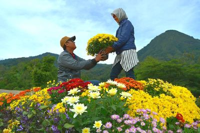 Side view of people standing by flowering plants against sky