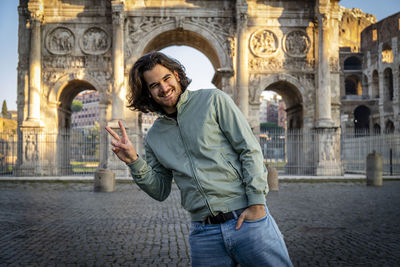 Young smiling man posing for a picture doing the v sign in front of the titus arch.