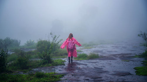 Rear view of woman wearing raincoat while standing on land during rainy season