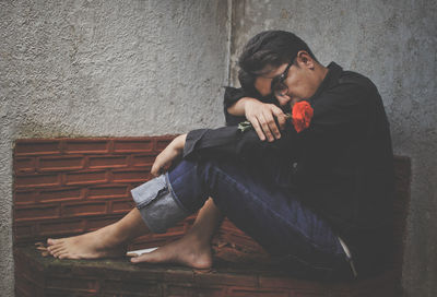 Sad man with rose while sitting by retaining wall