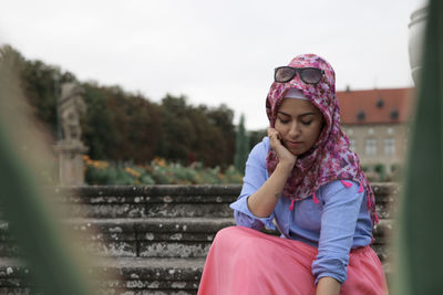 Young woman with hand on cheek looking down while sitting on steps