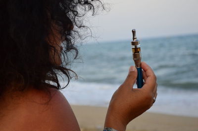 Close-up of woman holding electronic cigarette against sea