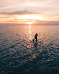 Silhouette person on sea against sky during sunset